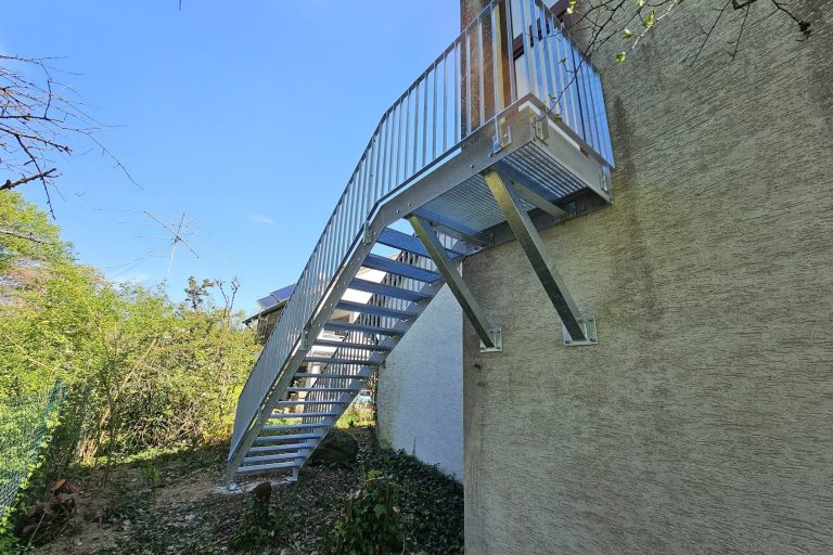 Eiserne Treppe, die an einer Wand nach draußen führt, umgeben von Bäumen und Sträuchern.
